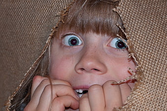 Close-up of frightened child peeking through torn burlap sack