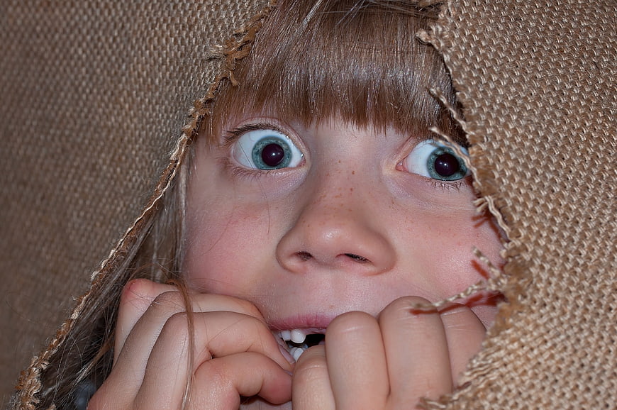 Close-up of frightened child peeking through torn burlap sack
