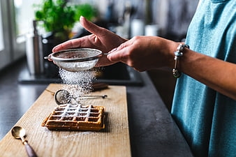 Woman sifting powdered sugar over waffle on wooden board