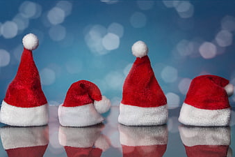 Four Santa Hats on Reflective Surface with Blue Bokeh Background