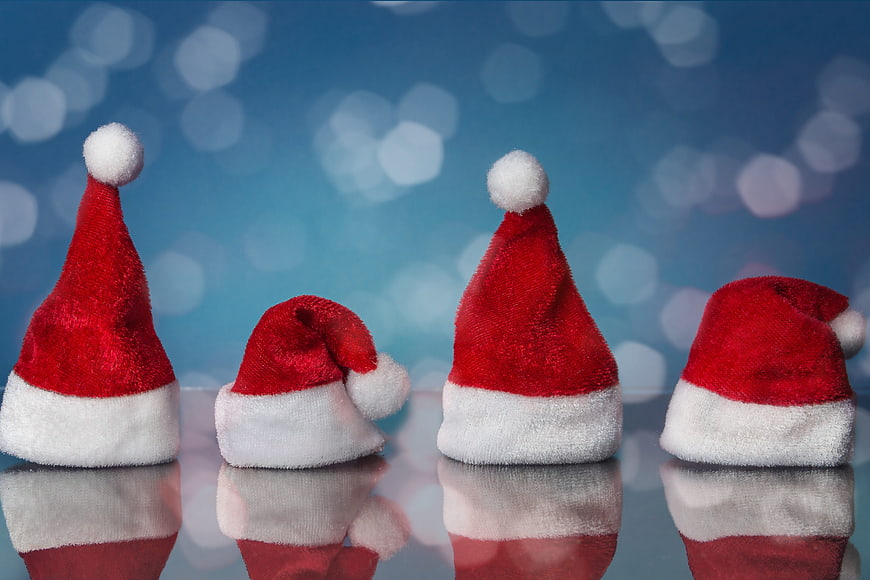 Four Santa Hats on Reflective Surface with Blue Bokeh Background