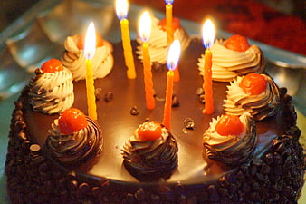Chocolate birthday cake with lit candles and cherries