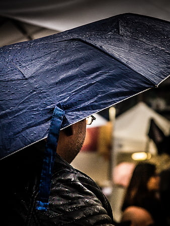 Man holding blue umbrella in rain with water droplets