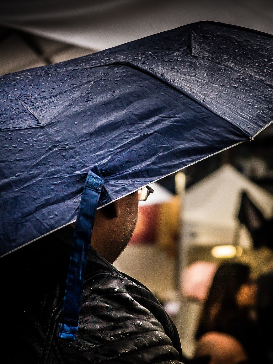 Man holding blue umbrella in rain with water droplets