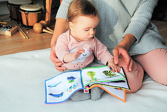 Baby reading soft book with mother on white blanket