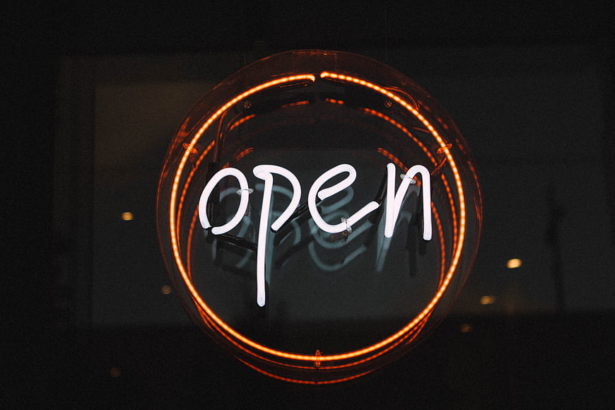 Circular Neon Open Sign Glowing In Dark Storefront Window