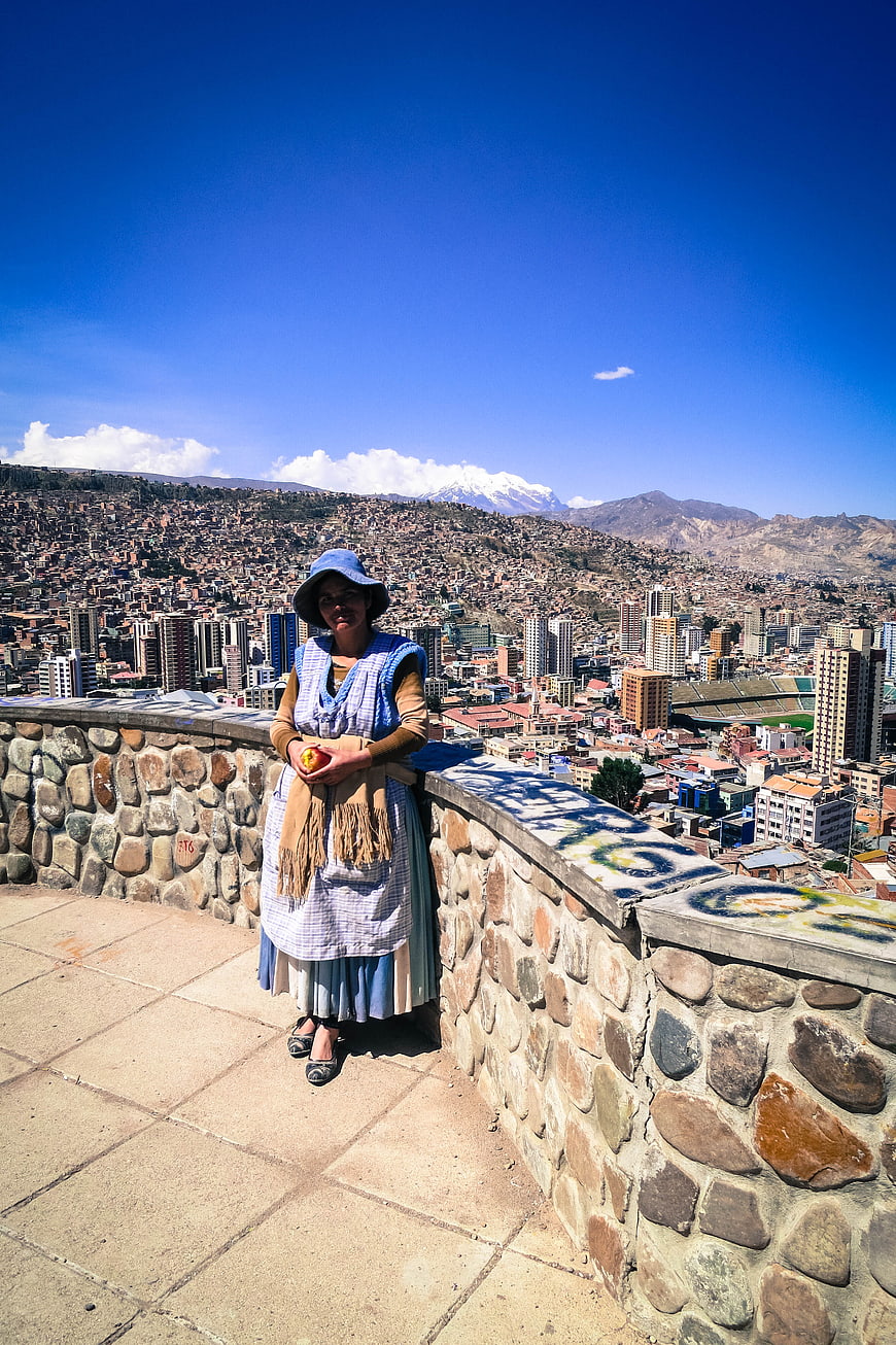 Woman in traditional dress overlooking La Paz cityscape