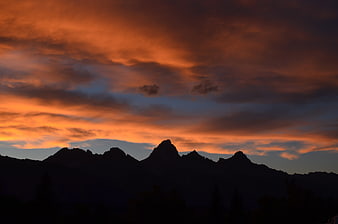 Dramatic orange sunset over dark mountain silhouette