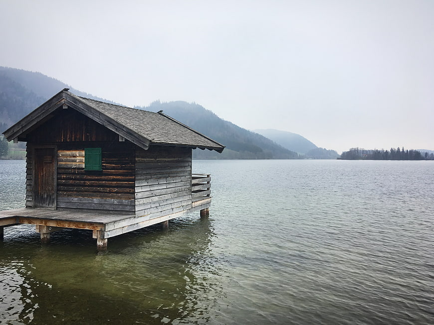 Rustic wooden boathouse on a misty lake with mountains
