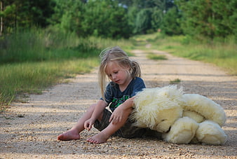 Young girl sitting on dirt road with large teddy bear