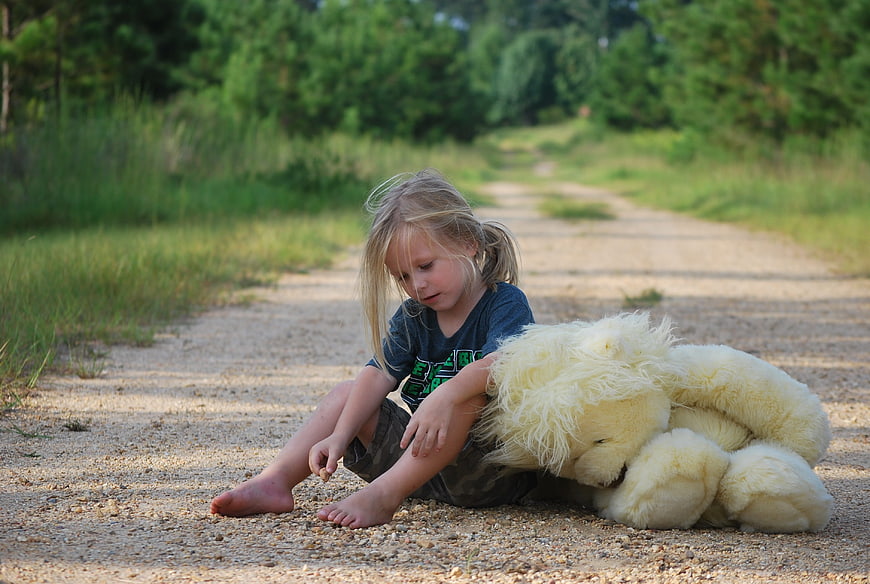 Young girl sitting on dirt road with large teddy bear