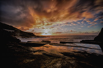 Dramatic sunset over rocky coastline with tide pools and bridge