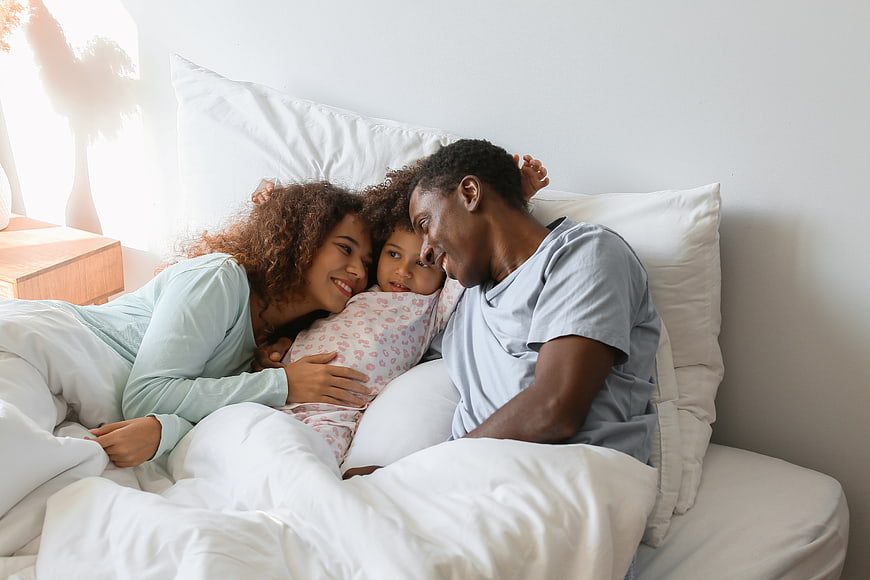 Happy African American Family Cuddling in Bed Together