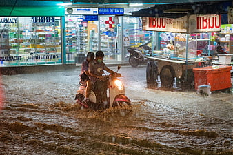 Couple riding scooter through flooded street in Thailand