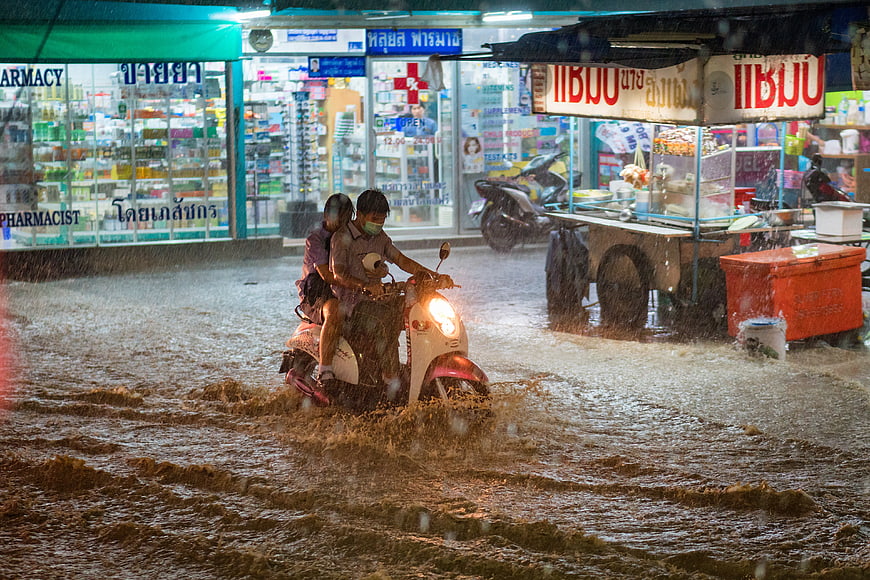 Couple riding scooter through flooded street in Thailand