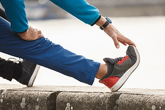 Senior man stretching leg on concrete ledge outdoors