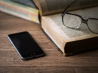 Smartphone and Reading Glasses on Open Book on Wooden Desk