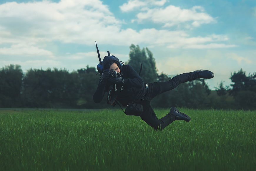 Man jumping in grassy field holding camera