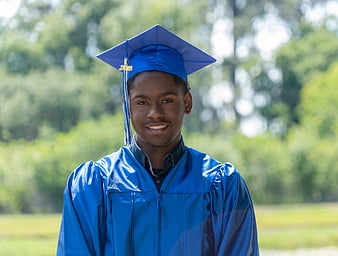 Smiling young African American male graduate in blue cap and gown outdoors