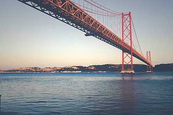Red suspension bridge over blue water at sunset