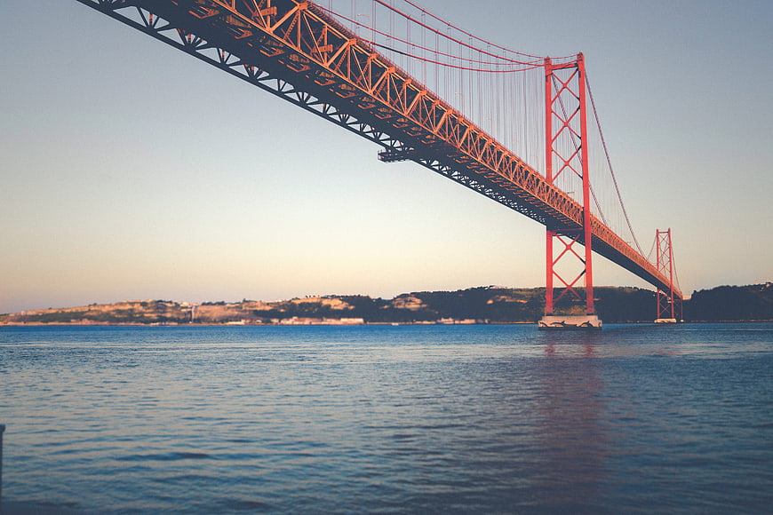 Red suspension bridge over blue water at sunset