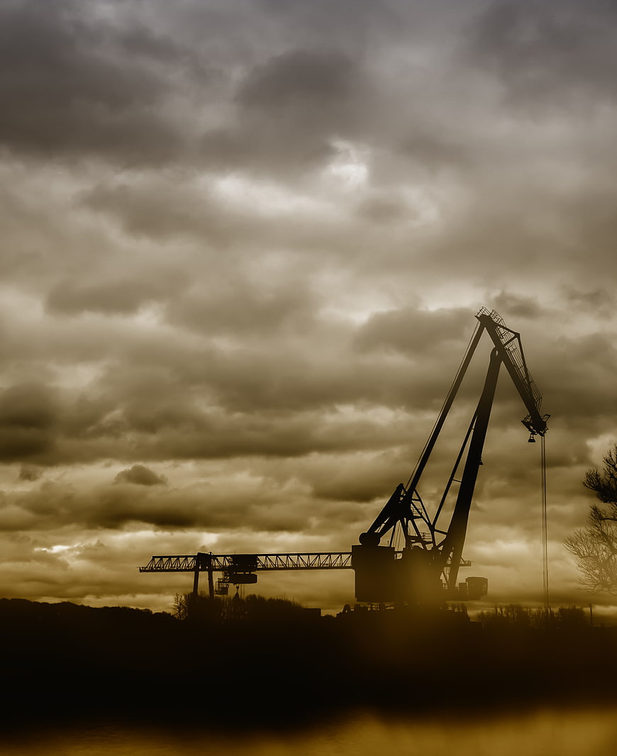 Silhouette of industrial cranes against dramatic cloudy sky