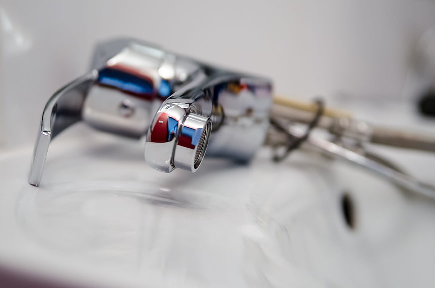 Close-up of chrome faucet with plumbing tools on white sink