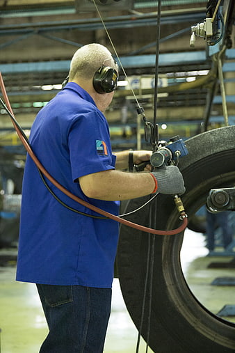 Factory Worker Operating Pneumatic Tool on Large Tire