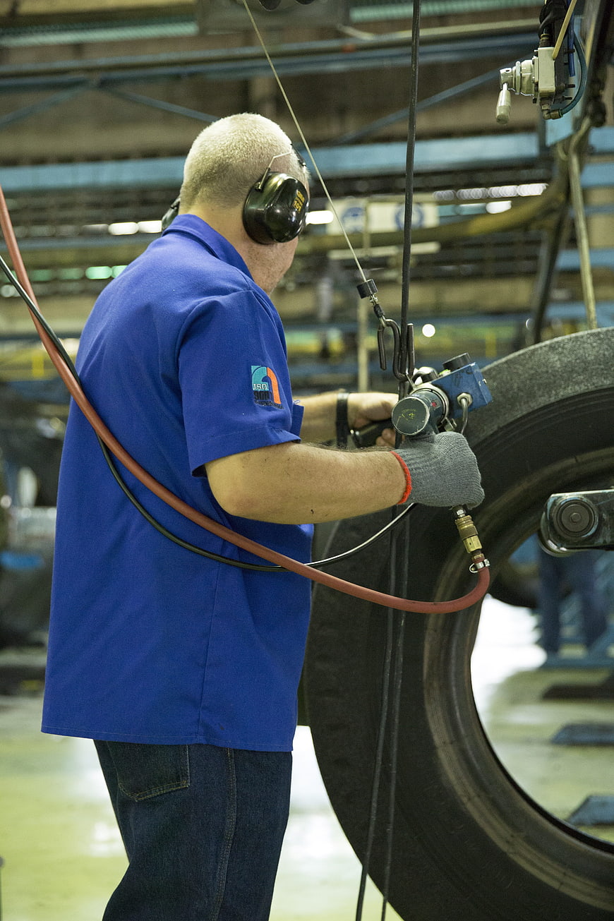 Factory Worker Operating Pneumatic Tool on Large Tire