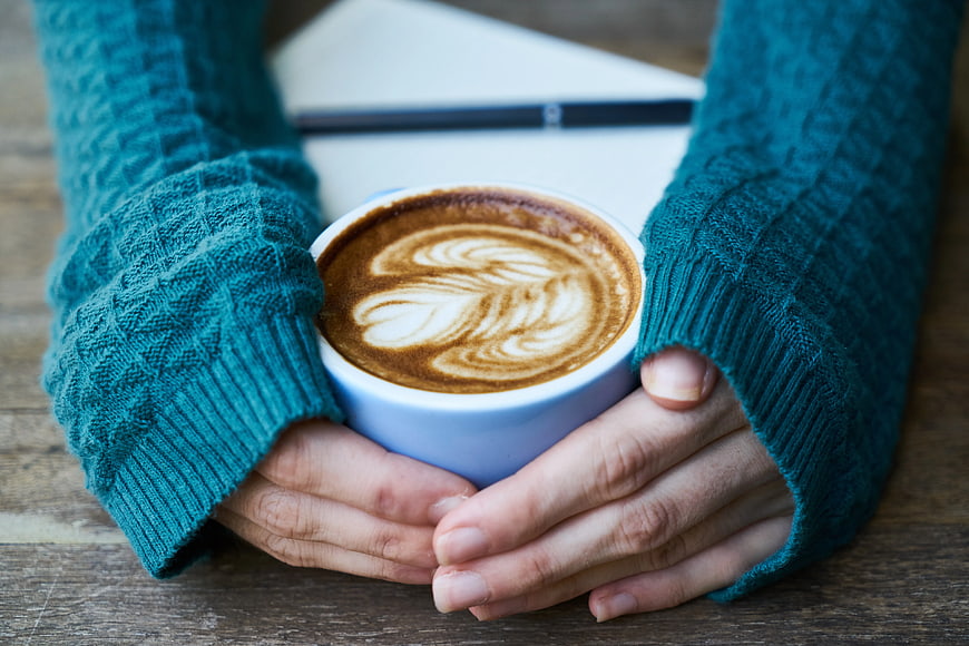 Hands holding latte art coffee cup in teal sweater