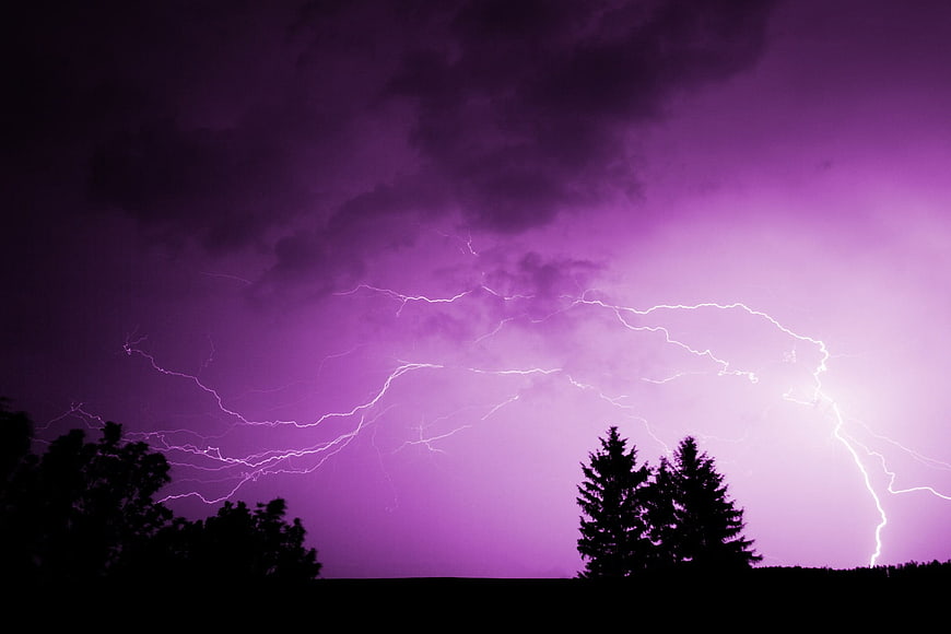 Dramatic purple lightning storm over silhouetted trees