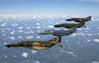Formation of four military fighter jets flying above clouds