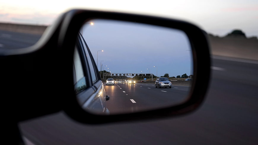 Highway traffic reflected in car side mirror at dusk