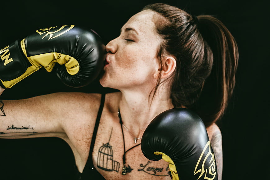 Female boxer kissing black and yellow boxing gloves in studio