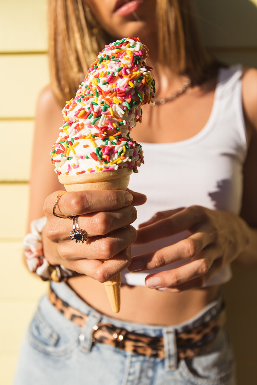 Woman holding colorful sprinkled ice cream cone in sunlight
