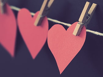 Red paper hearts hanging on clothesline with wooden pegs
