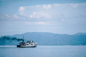 Ferry boat crossing calm blue sea with distant mountains and cloudy sky