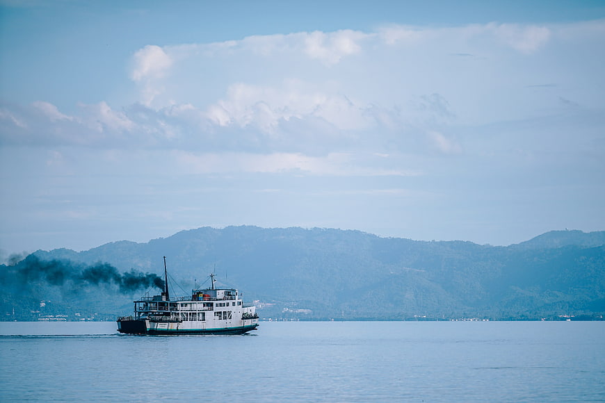 Ferry boat crossing calm blue sea with distant mountains and cloudy sky