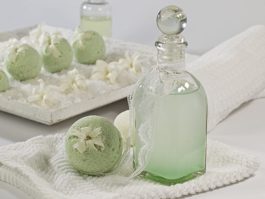 Green bath bombs and perfume bottle on white towel