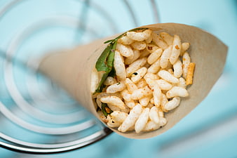 Spicy puffed rice snack in paper cone on blue background