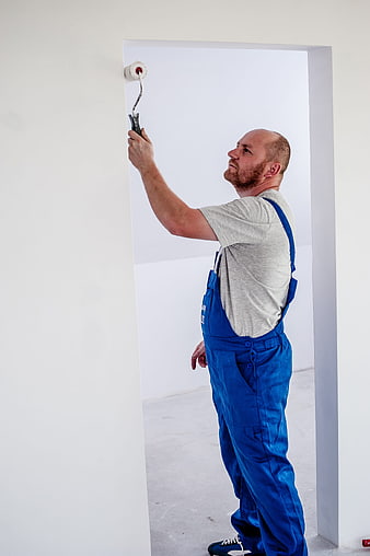 Painter in Blue Overalls Painting White Wall with Roller