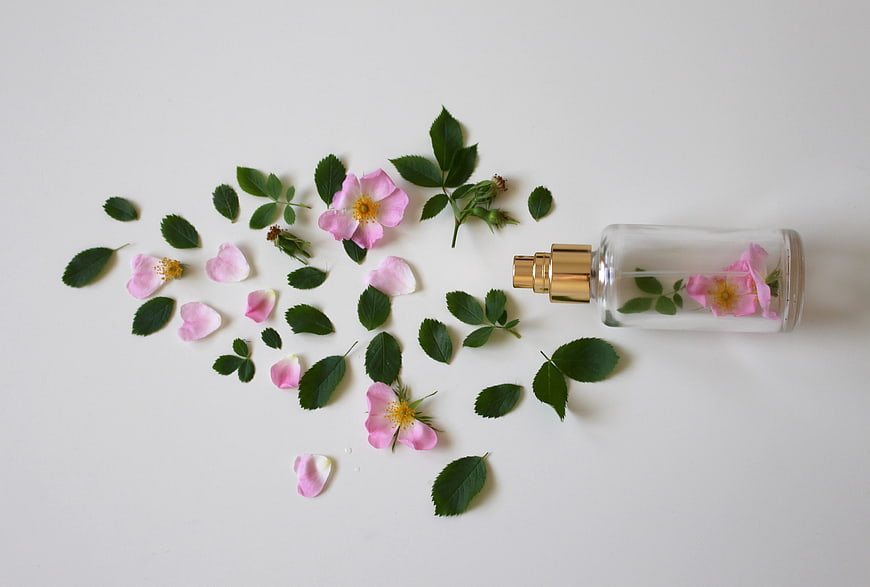 Rose perfume bottle with petals and leaves on white background