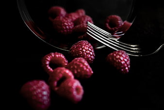 Dark moody raspberries spilling from glass bowl with fork