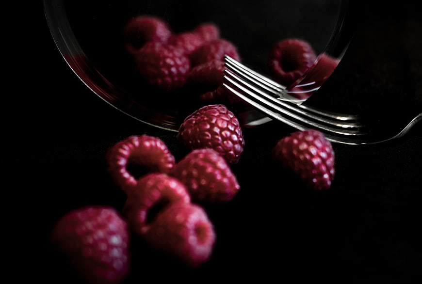 Dark moody raspberries spilling from glass bowl with fork