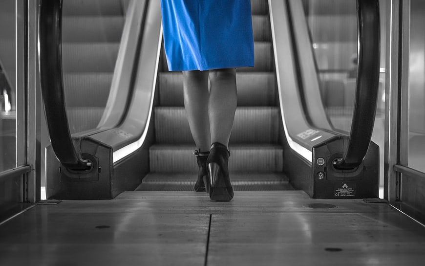 Woman in Blue Dress Walking Up Escalator