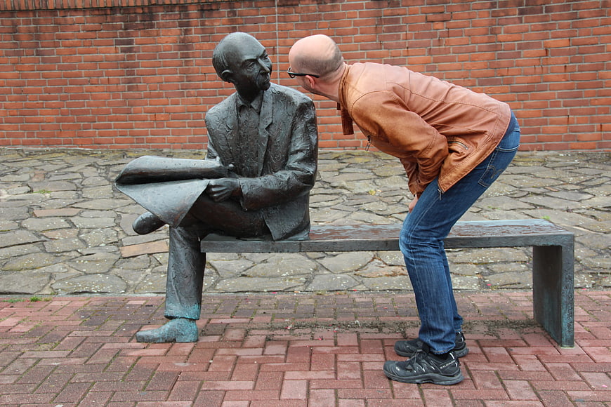 Man whispering to bronze statue on bench