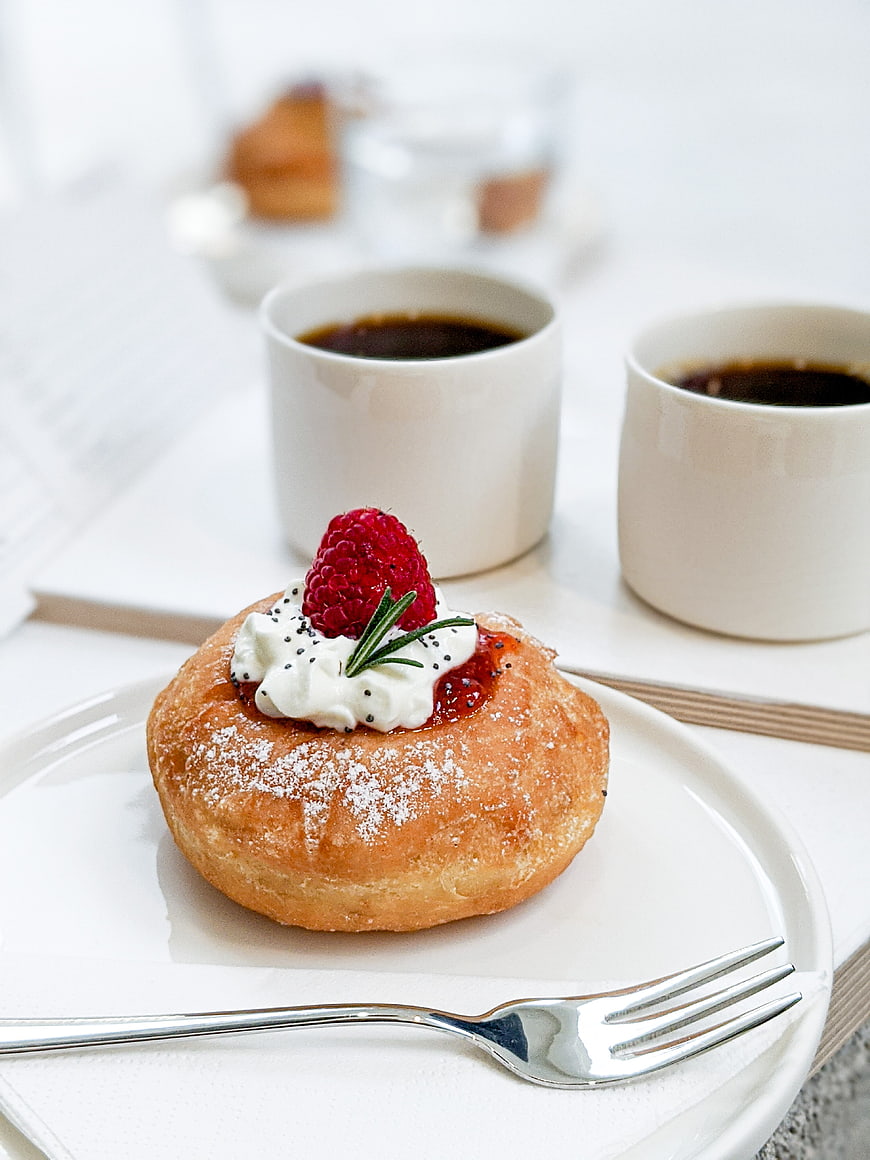 Raspberry cream donut with coffee on white table