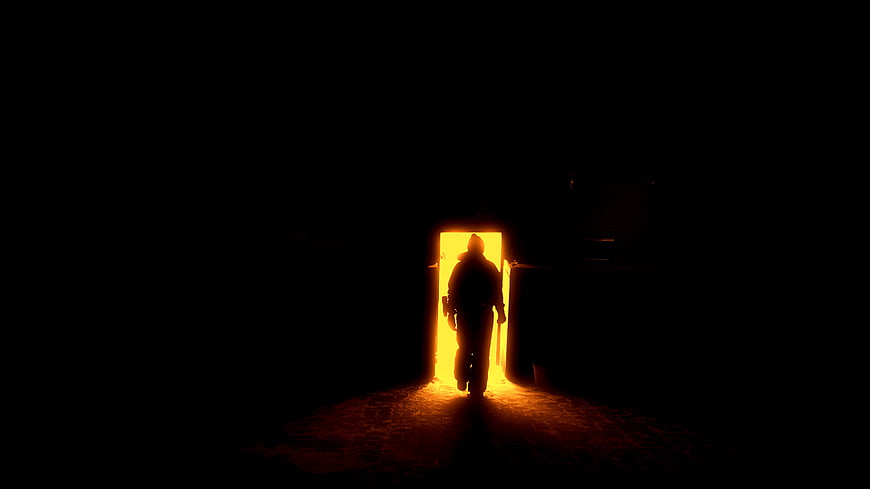 Silhouette of person walking through glowing doorway in darkness