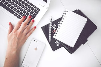 Flat lay of female hand typing on laptop with notebook and smartphone