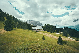 Alpine wooden cabin on grassy hill with mountains